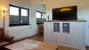 Ein Wohnzimmer mit Fernseher, einem Tisch mit Glas, einem Sessel und einer Schrankwand mit Regalen.