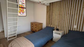 A bedroom with two beds, a wooden dresser, a ladder, and a stained glass window.