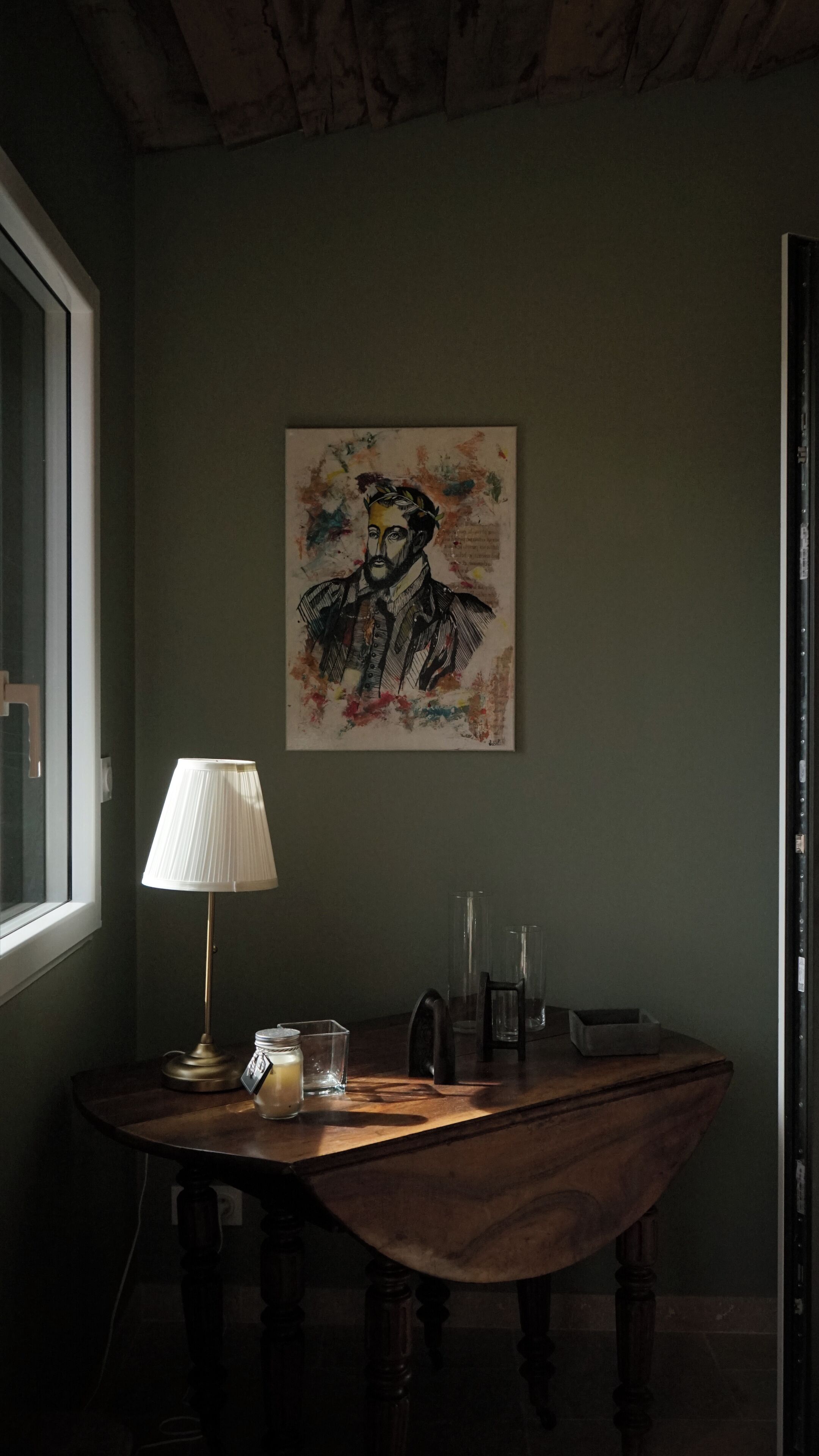 Een kamer met een houten tafel, een lamp en een schilderij aan de muur.