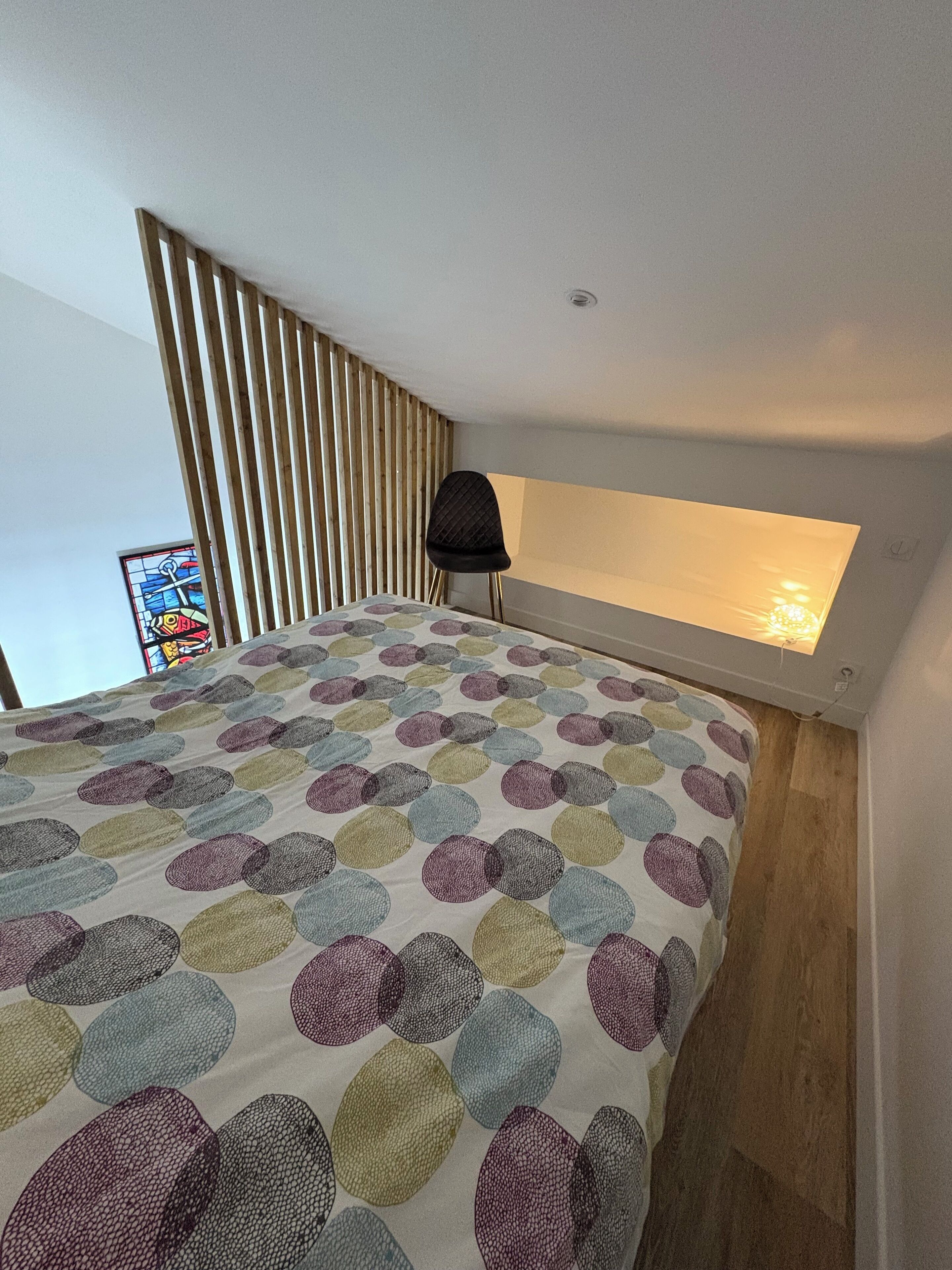 Een slaapkamer met een bed, een raam en een wandlamp.
