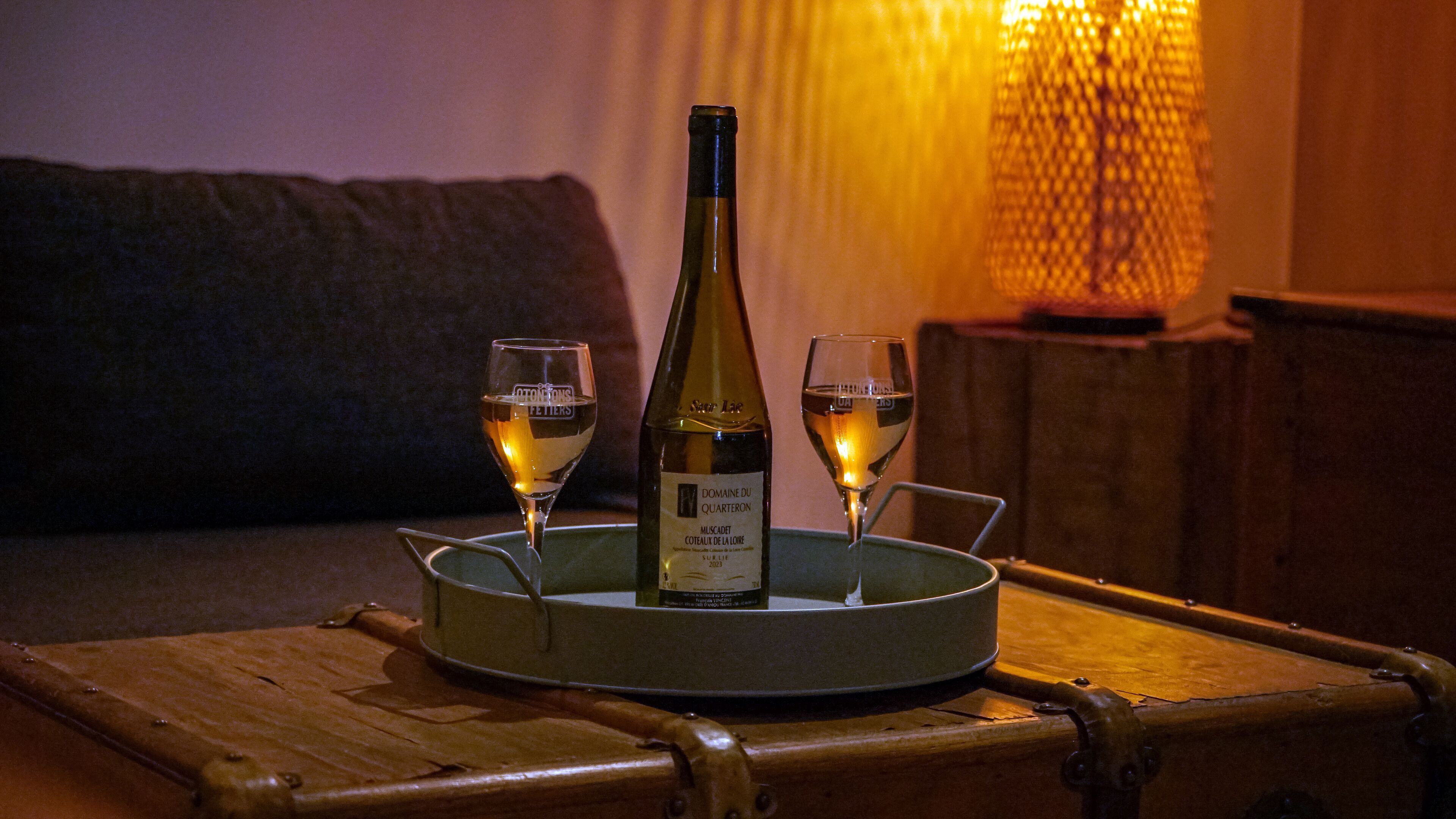 A bottle of wine on a tray with two glasses filled with wine, placed on a wooden table in a dimly lit room.