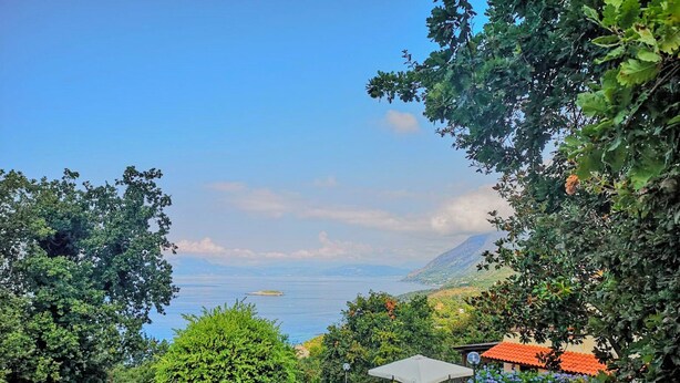 A scenic outdoor area with a stone pathway leading to a seating area with umbrellas, surrounded by lush greenery and overlooking a body of water. - Villa Rosamaria (Maratea)