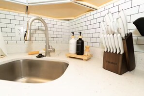 Een keuken met een rvs-spoelbak, een witte betegelde achterwand en een messenblok op het aanrecht.