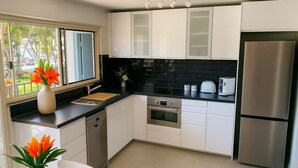 Eine moderne Küche mit weißen Schränken, einer schwarzen Rückwand, Edelstahlgeräten und einem Fenster mit Blick ins Freie.