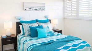 Ein ordentlich bezogenes Bett mit blauer und weißer Streifenoptik, zwei Nachttischlampen und ein gerahmtes Bild an der Wand darüber.
