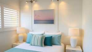Une chambre à coucher bien rangée, avec un lit, des oreillers, des lampes de chevet et un tableau accroché au mur.