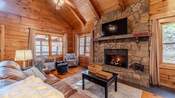 L’intérieur d’une cabane en rondins, avec une cheminée en pierre, des meubles en cuir et un téléviseur fixé au-dessus.