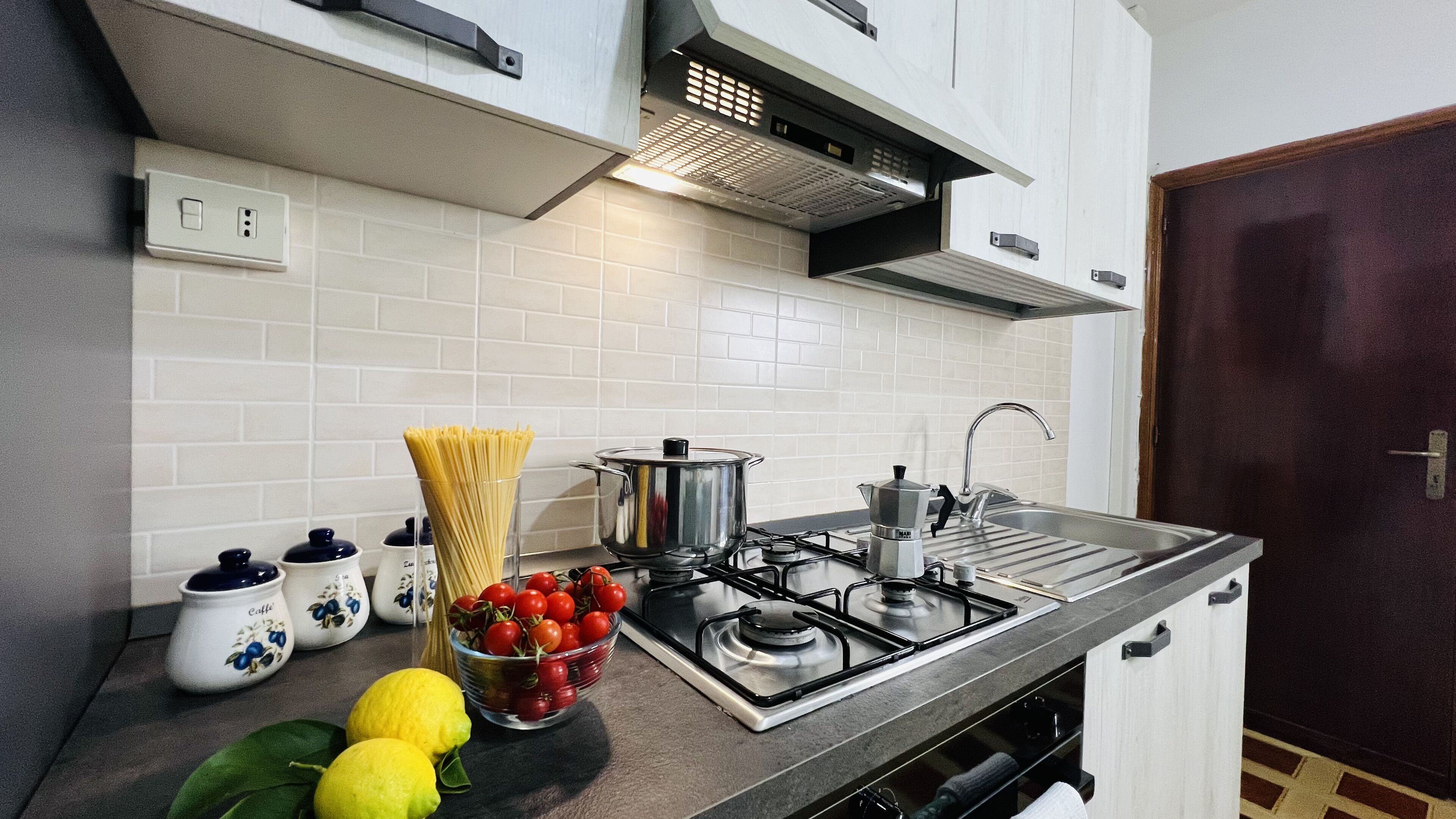 Une cuisine moderne avec des armoires blanches, une cuisinière en acier inoxydable et un évier. On peut voir des citrons et des tomates frais sur le comptoir.