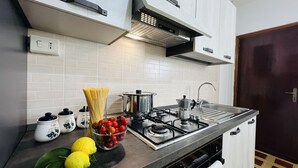 A modern kitchen with white cabinets, a stainless steel stove, and a sink. There are fresh lemons and tomatoes on the counter. - Cozy Apartment in Center of Tropea, 5 min from Station, free parking (Tropea)