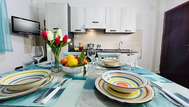 A modern kitchen with white cabinets, a built-in oven, and a dining area with striped tableware and a vase of flowers. - Cozy Apartment in Center of Tropea, 5 min from Station, free parking (Tropea)