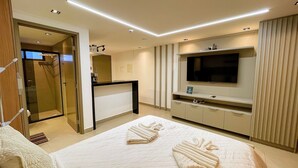 Una habitación de hotel moderna con cama, televisor, escritorio y zona de ducha.