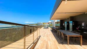 Un bar en la azotea con terraza de madera, baranda de vidrio y asientos al aire libre.