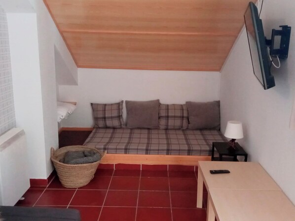 A small, cozy room with a sloped ceiling, a bed with plaid bedding, a small table with a lamp, and a television mounted on the wall. - Apartamentos Las Tuyas 3000 (Monachil)