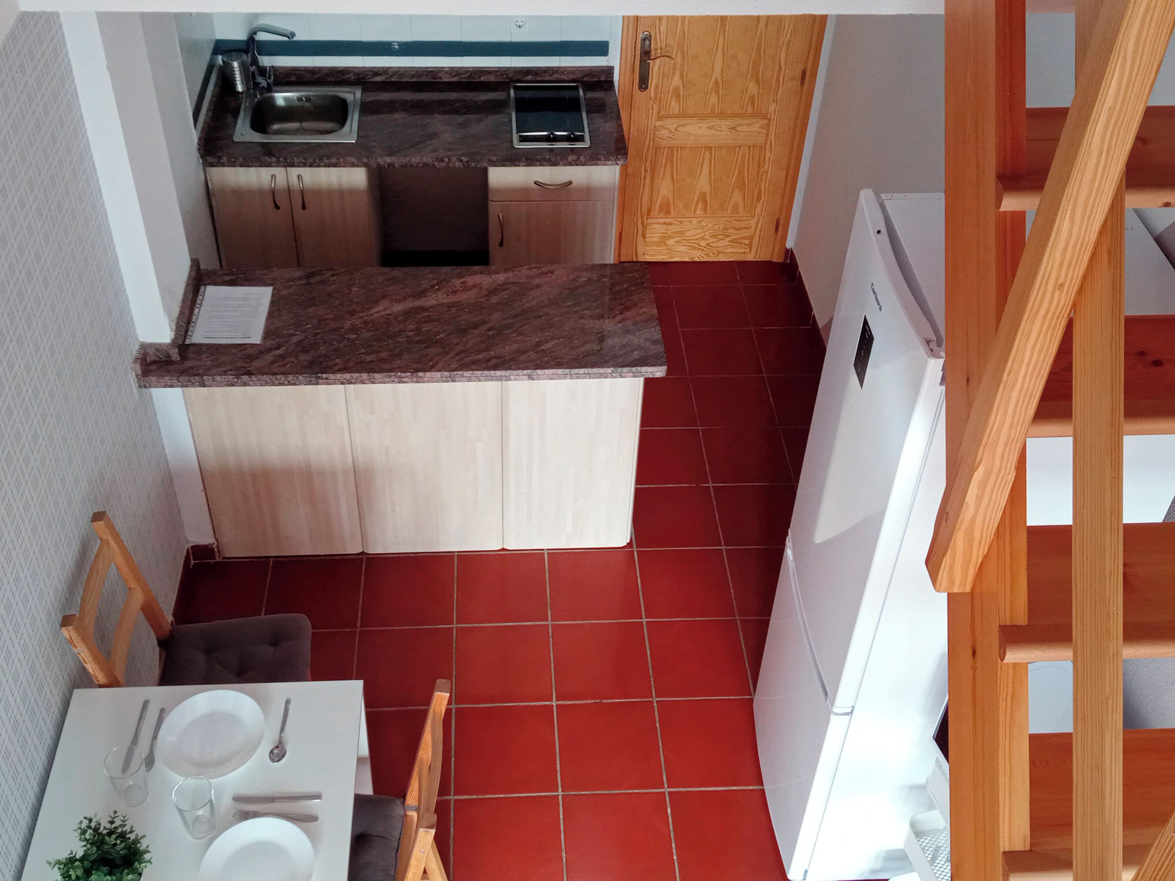 Una cocina compacta con un lavamanos, armarios de madera, un refrigerador blanco y una zona de comedor con una mesa dispuesta para dos.