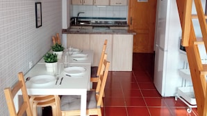 A compact kitchen with a dining area, wooden cabinets, a refrigerator, and a small table set for two.