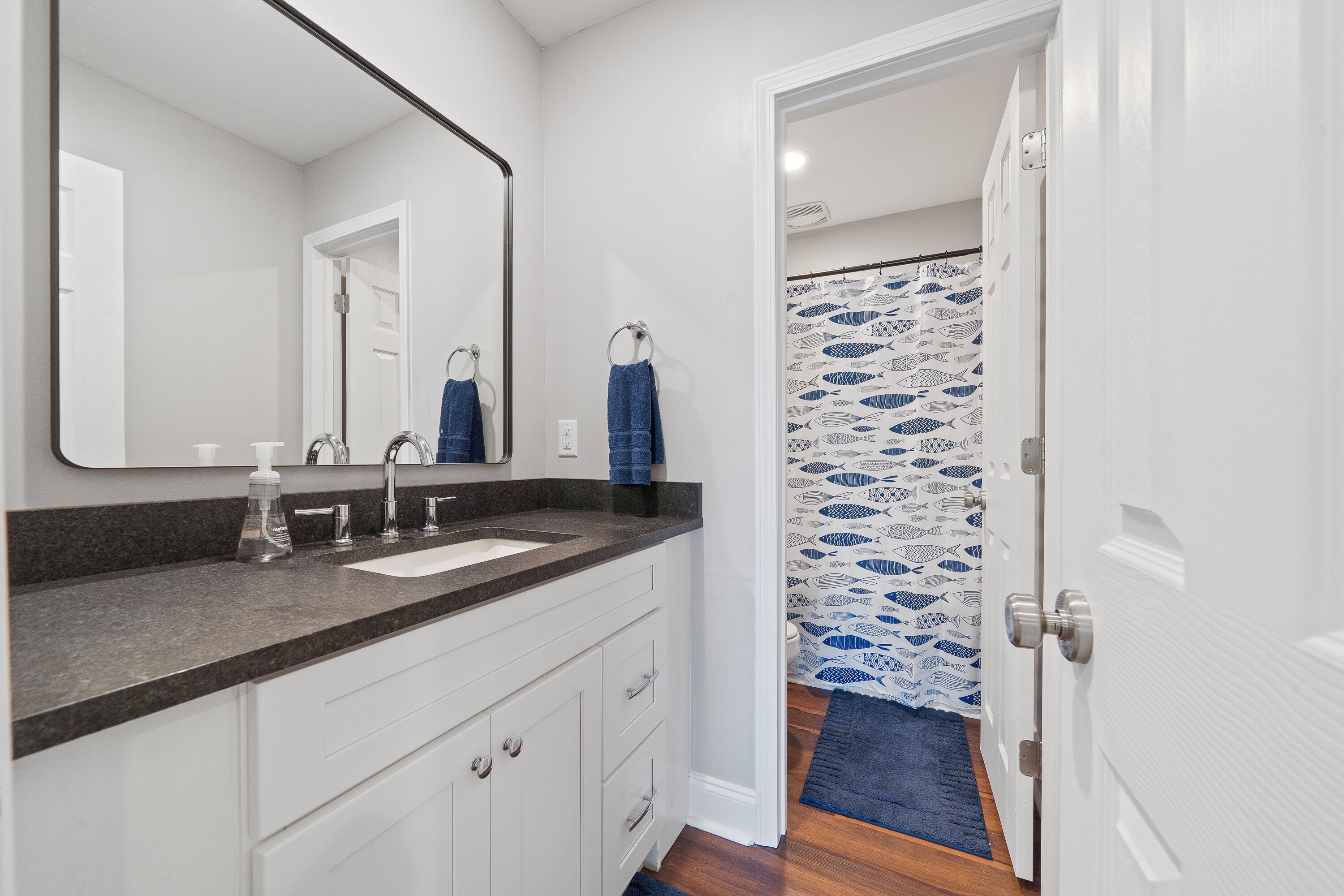 A bathroom with a double sink, a mirror, a towel rack, and a shower with a blue and white fish pattern.
