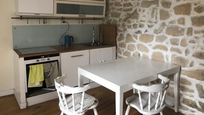 A compact kitchen with a stone wall, wooden cabinets, a white countertop, and a dining table with two chairs. - Very charming 1 bed room in heart of paris with balcony (Paris)