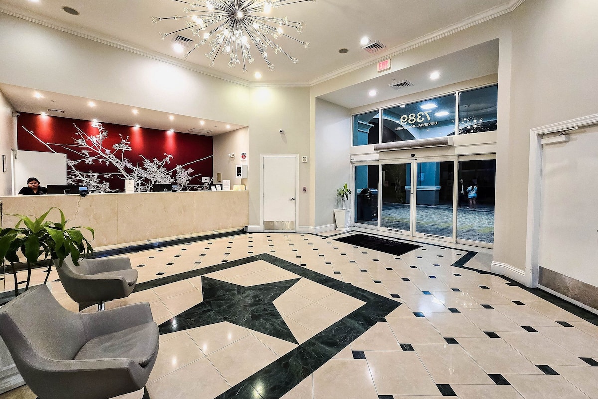 A hotel lobby with a reception desk, a large star-patterned floor, and a modern chandelier.