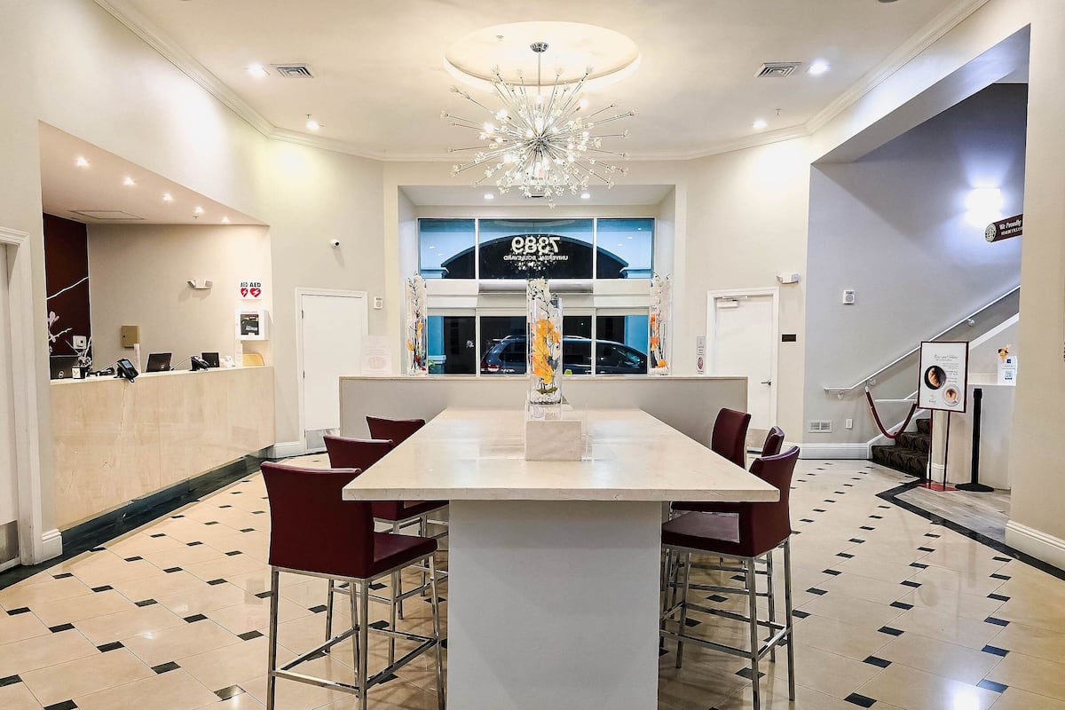 A hotel lobby with a reception desk, a large chandelier, and a view of the outside through the windows.