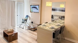 Un coin repas avec une table mise pour le repas, un transat pour bébé et un téléviseur diffusant une émission.