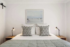 Ein Schlafzimmer mit einem Bett, zwei Nachttischen mit Lampen, einem gerahmten Bild an der Wand und gemusterten Kissen.