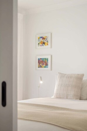 A bedroom with a bed, two framed abstract paintings, a bedside lamp, and a door. - Bayside—Serene Haven near the Town Centre & Beach (Dunsborough)