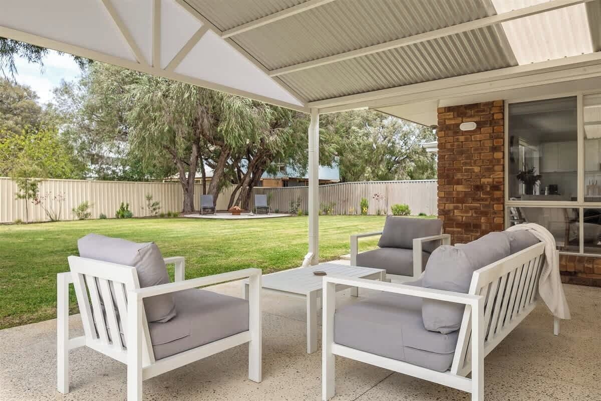 A covered outdoor seating area with white furniture and a brick wall.