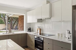 A modern kitchen with white cabinets, a built-in oven, and a large window. - Bayside—Serene Haven near the Town Centre & Beach (Dunsborough)