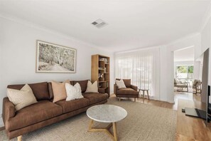 Ein modernes Wohnzimmer mit einem braunen Sofa, einem runden Couchtisch, einem Bücherregal und einem Bild an der Wand.