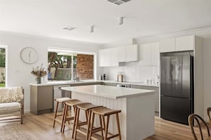 A modern kitchen with a central island, white cabinetry, and a stainless steel refrigerator. - Bayside—Serene Haven near the Town Centre & Beach (Dunsborough)