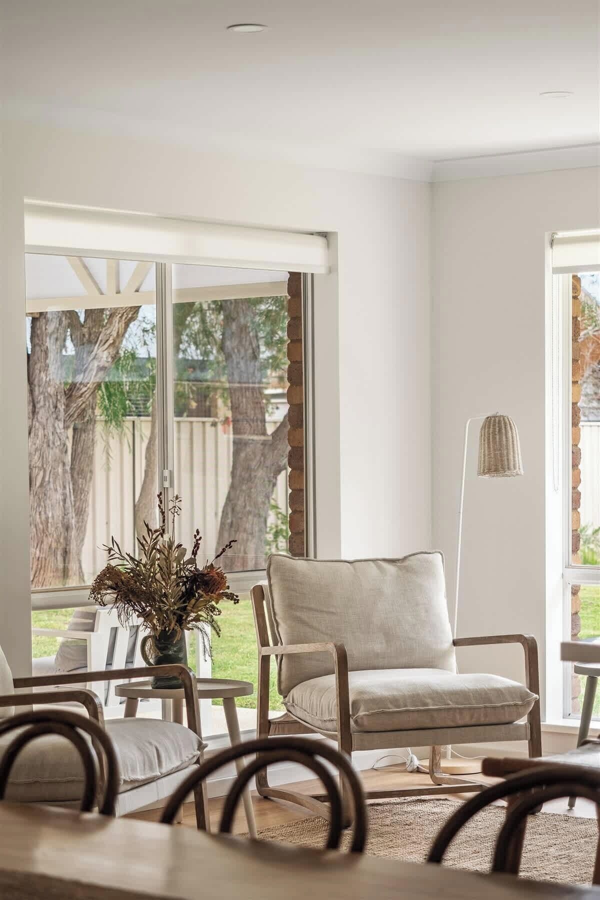 Una habitación con un ventanal grande, una silla, una mesa y una lámpara de pie.