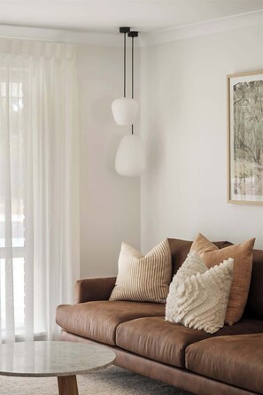 A living room with a brown leather sofa, a round coffee table, and a painting on the wall. - Bayside—Serene Haven near the Town Centre & Beach (Dunsborough)