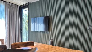 Un comedor moderno con una mesa de madera, sillas de mimbre y un televisor de pantalla plana montado en una pared verde con textura.