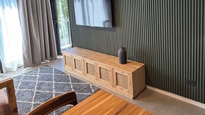 Una sala de estar moderna con una mesa de comedor de madera, un televisor montado en una pared con textura y un mueble de madera empotrado.