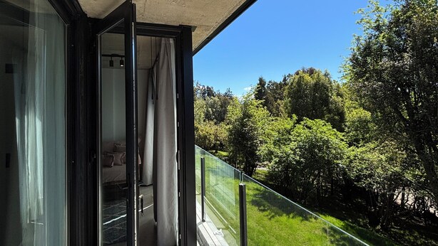 Un balcón con puerta de vidrio que da a un dormitorio, techo de hormigón y vista a un paisaje verde.