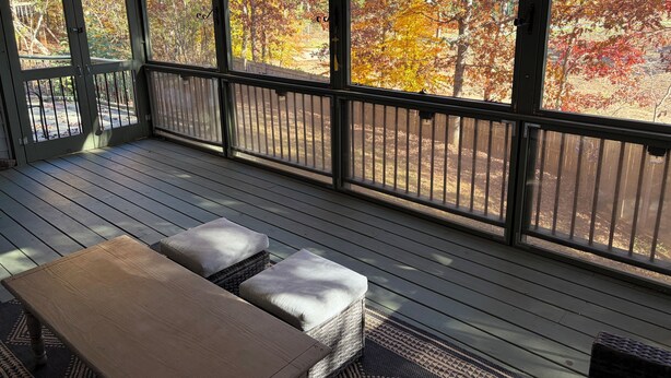 A covered outdoor deck with a table and cushioned seating, overlooking a yard with autumn foliage. - Peaceful Two Bedroom Apartment in Charming Weaverville. (Weaverville)