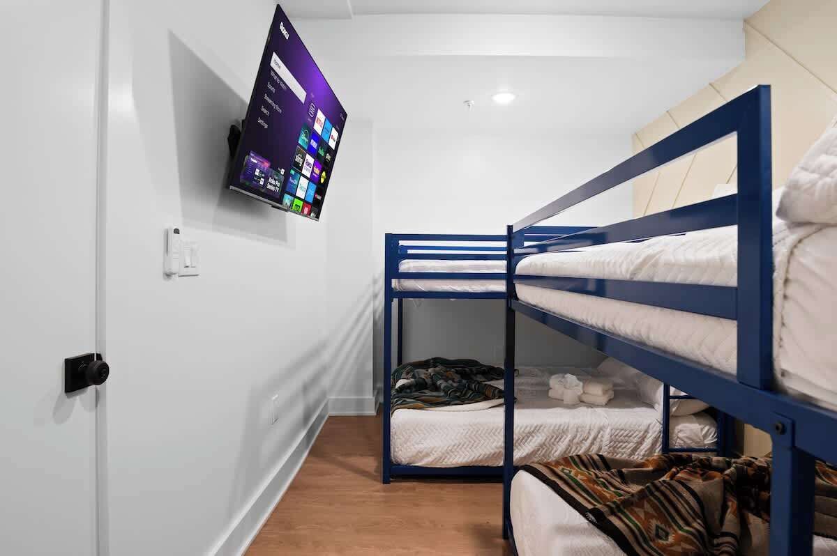 A bunk bed room with a TV mounted on the wall, a door with a lock, and a wooden floor.