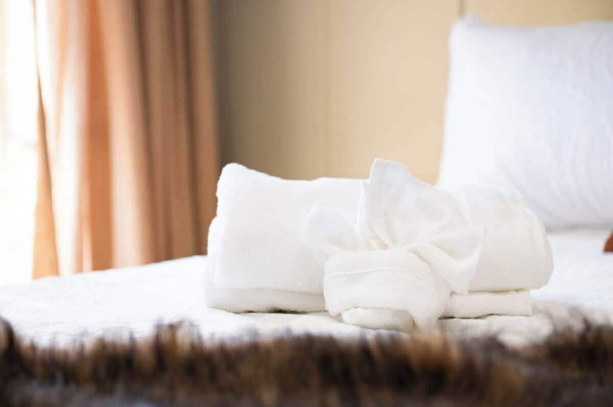 Une serviette blanche, soigneusement pliée, est posée sur un lit recouvert d’une couverture qui ressemble à de la fourrure.