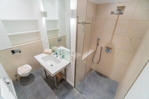 Et badeværelse med toilet, vask, spejl og brusebad.