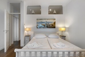 Une chambre à coucher avec un lit double, deux lampes de chevet, un tableau au-dessus du lit et une porte donnant sur une autre pièce.