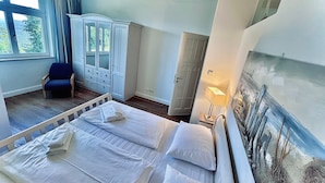 Een slaapkamer met een groot bed, een stoel, een kledingkast en een schilderij aan de muur.