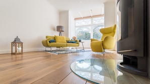 Een moderne woonkamer met een glazen salontafel, houten vloeren en gele fauteuils.