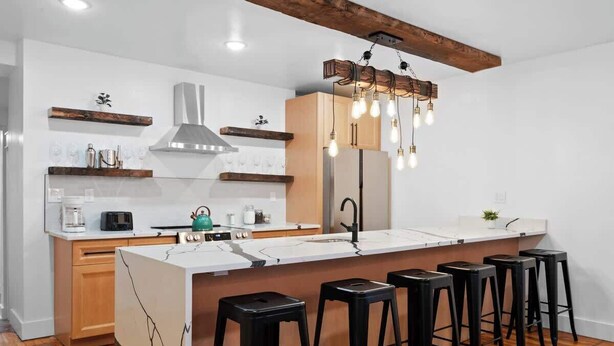 Eine moderne Küche mit einer zentralen Kochinsel, Holzbarhocker und einer außergewöhnlichen Leuchte.