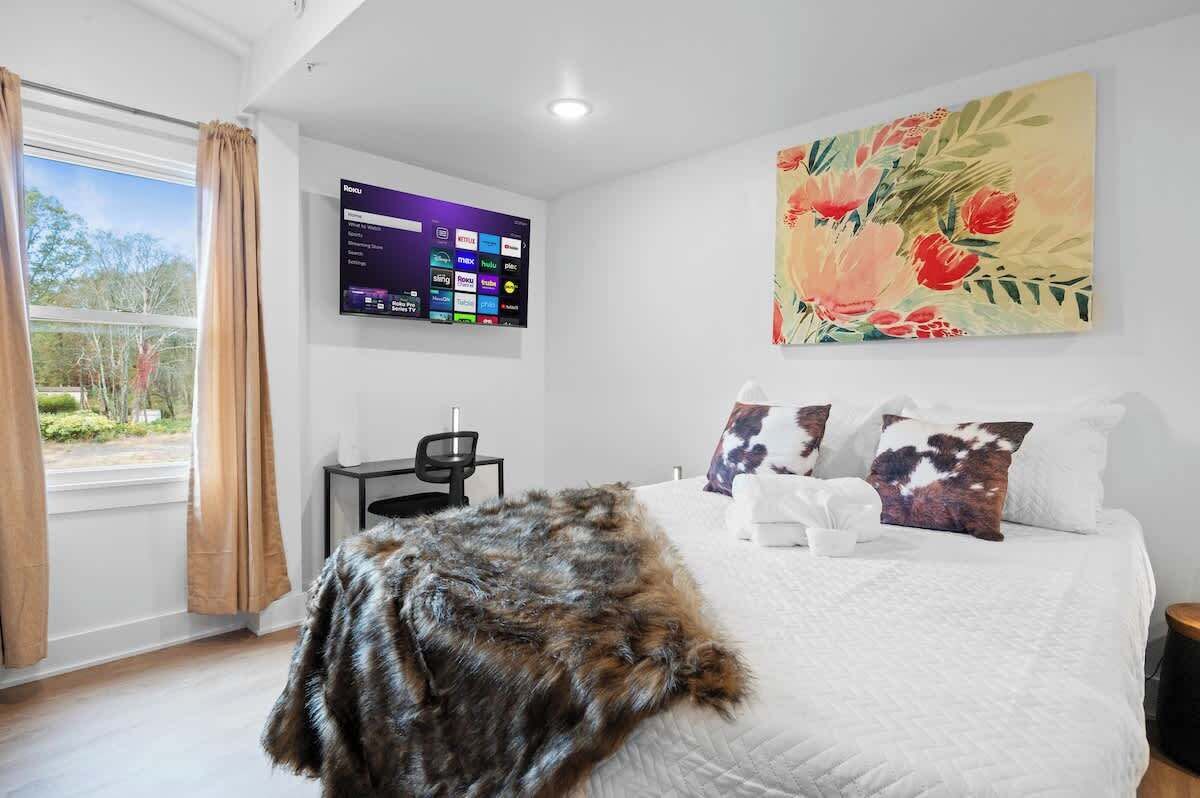 Un dormitorio con una cama grande, un televisor montado, un cuadro y vistas al exterior.