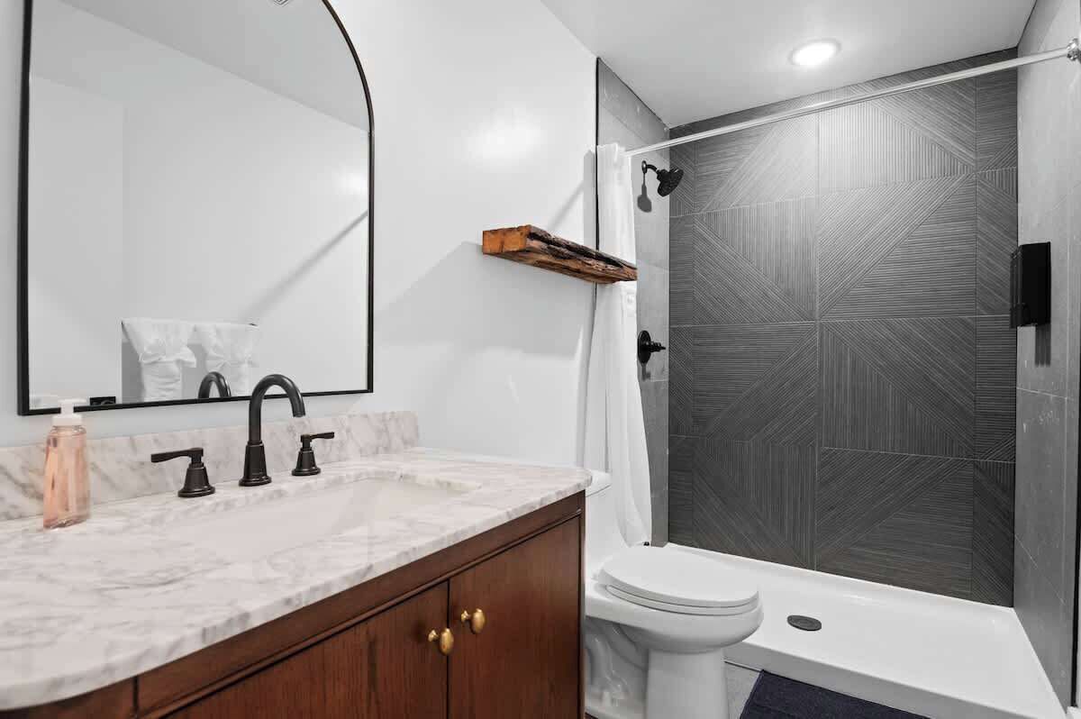 A modern bathroom with a marble sink, a toilet, and a shower with a geometric tile wall.