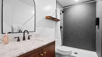 A modern bathroom with a marble sink, a toilet, and a shower with a geometric tile wall.