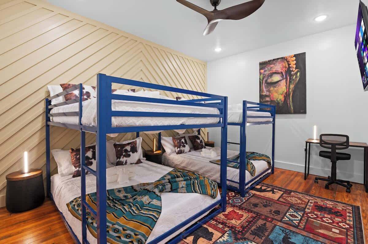 Une chambre avec un lit superposé, un ventilateur de plafond, un tableau au mur et un bureau avec une chaise.
