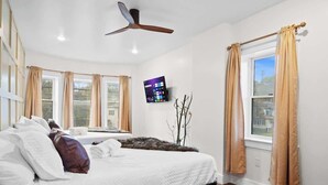 A bedroom with a bed, a ceiling fan, a TV on the wall, and windows with curtains. - Lakeside Serenity Retreat Near Kalahari Resort (Pocono Summit)