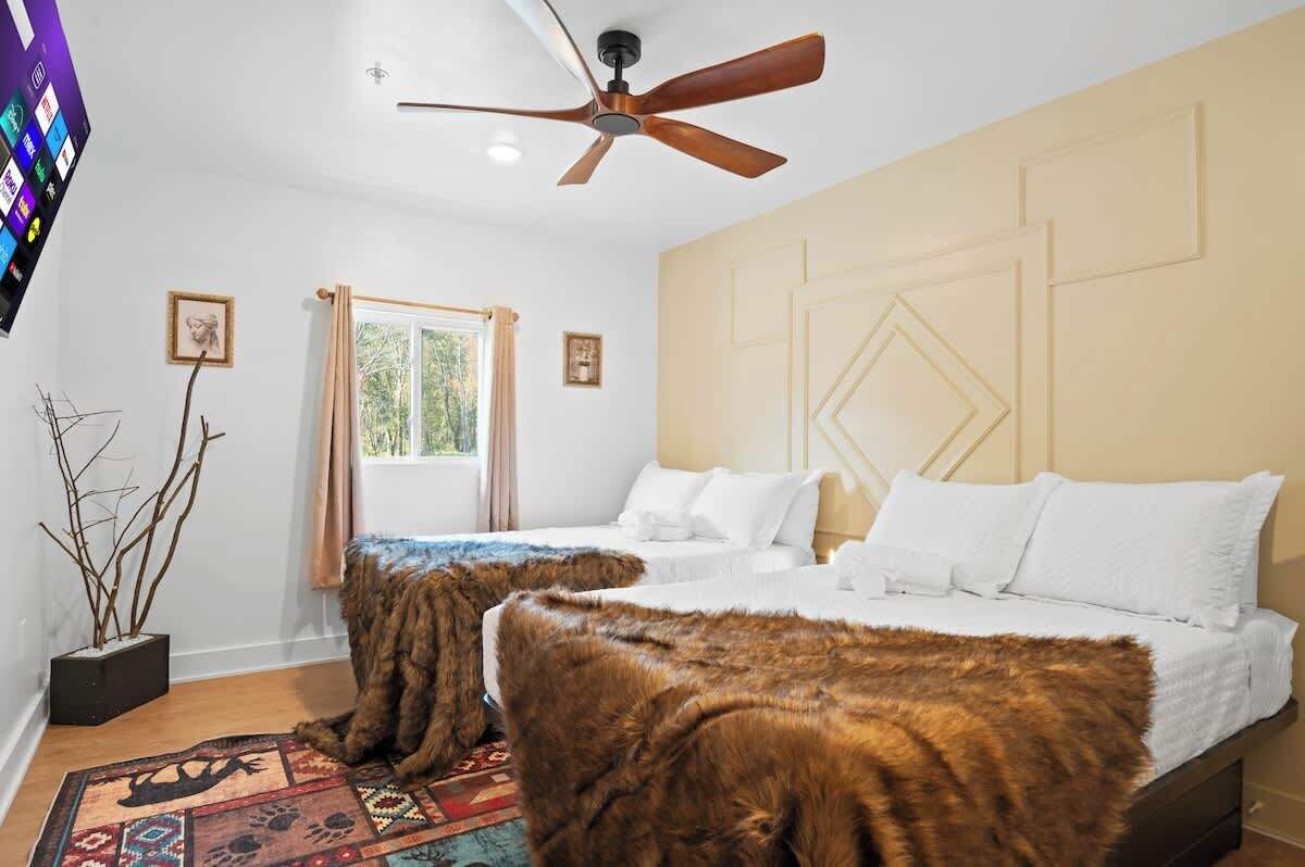 Ein Schlafzimmer mit zwei Betten, einem Deckenventilator, einem Fernseher und einem Fenster mit Vorhängen.