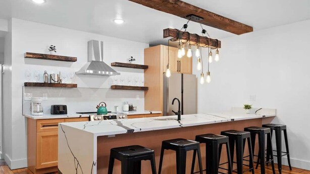 Una cocina moderna con una isla central, taburetes de bar, vigas de madera e iluminación colgante.